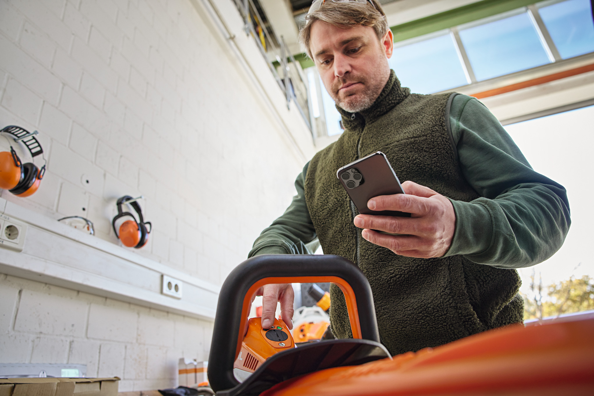 Osoba sprawdzająca status urządzenia na Smart Connector 2 A i przeglądająca je na smartfonie za pomocą aplikacji STIHL connected App