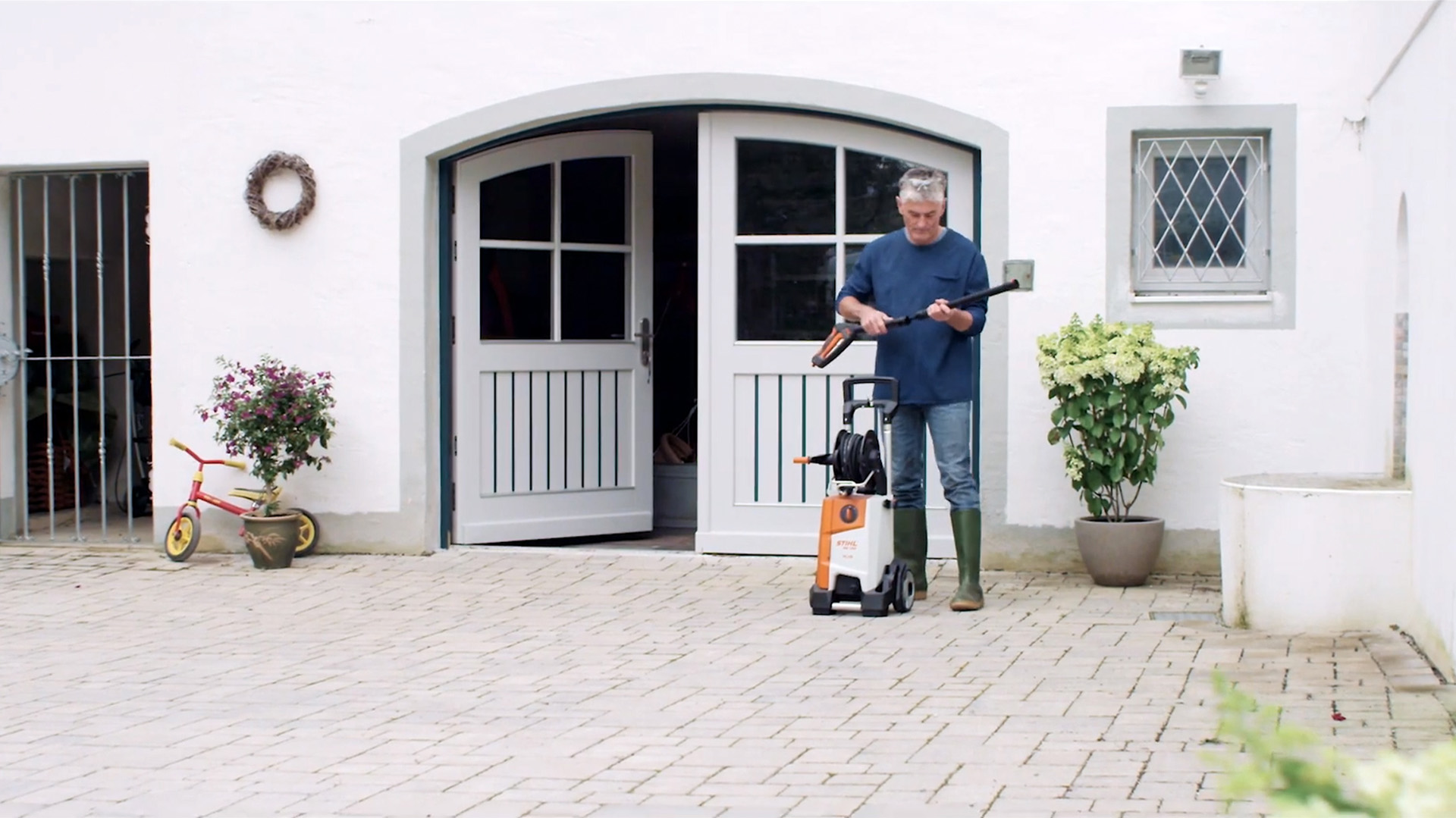 Mężczyzna stoi przed białym domem i przygotowuje myjkę wysokociśnieniową STIHL do czyszczenia elewacji