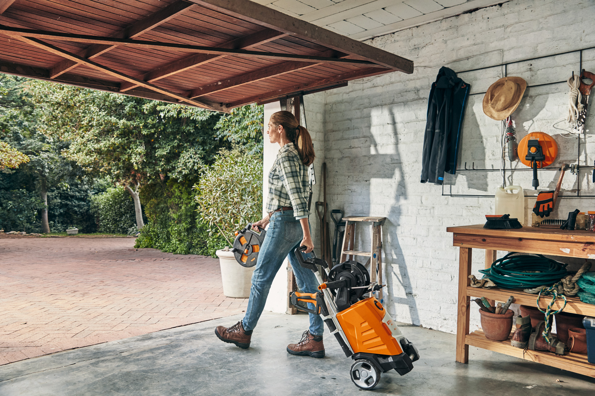 Kobieta wychodząca z garażu z myjką wysokociśnieniową STIHL RE 130 PLUS, której zamierza użyć