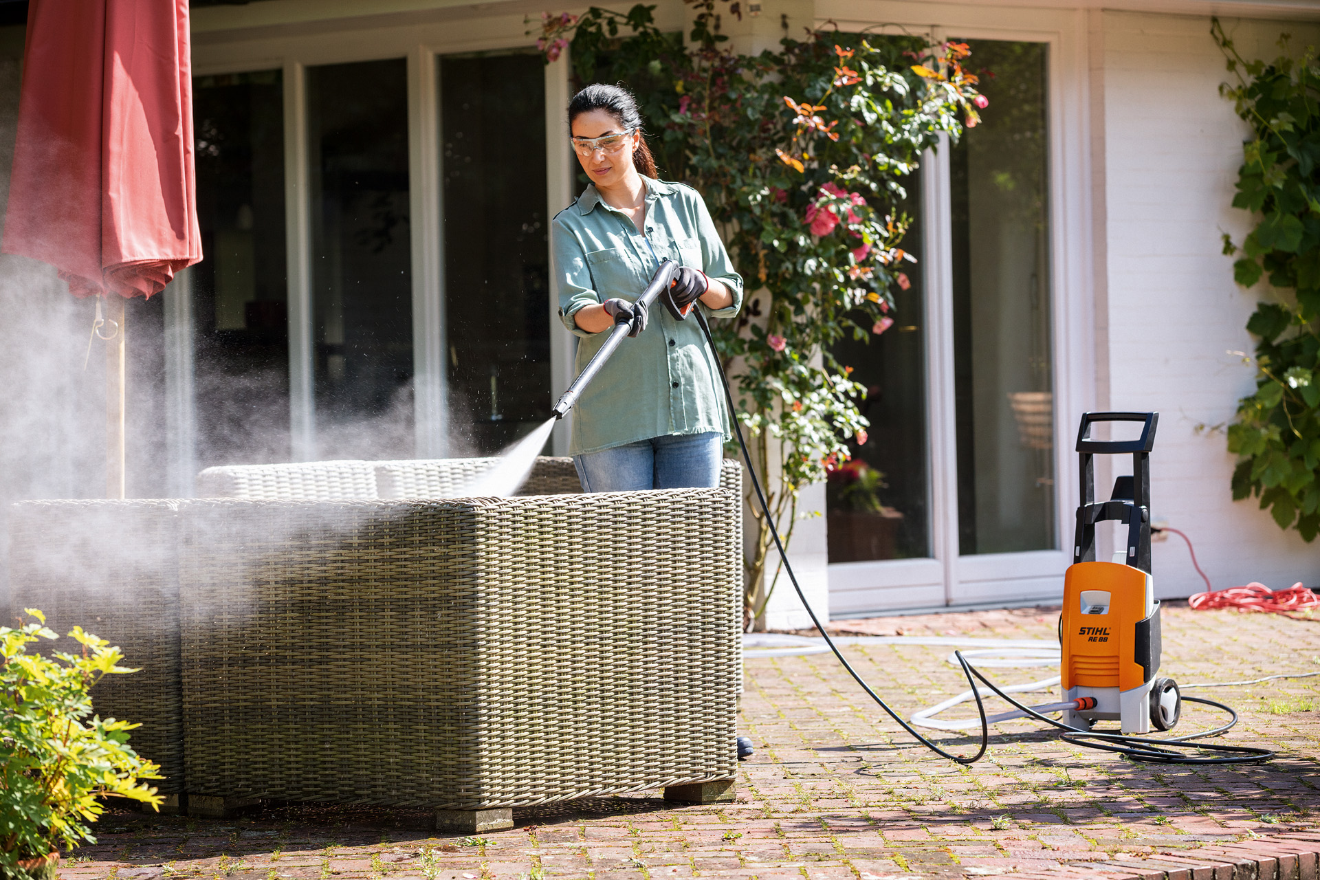 Kobieta w okularach ochronnych czyszcząca meble ogrodowe myjką wysokociśnieniową STIHL RE 88 na tarasie