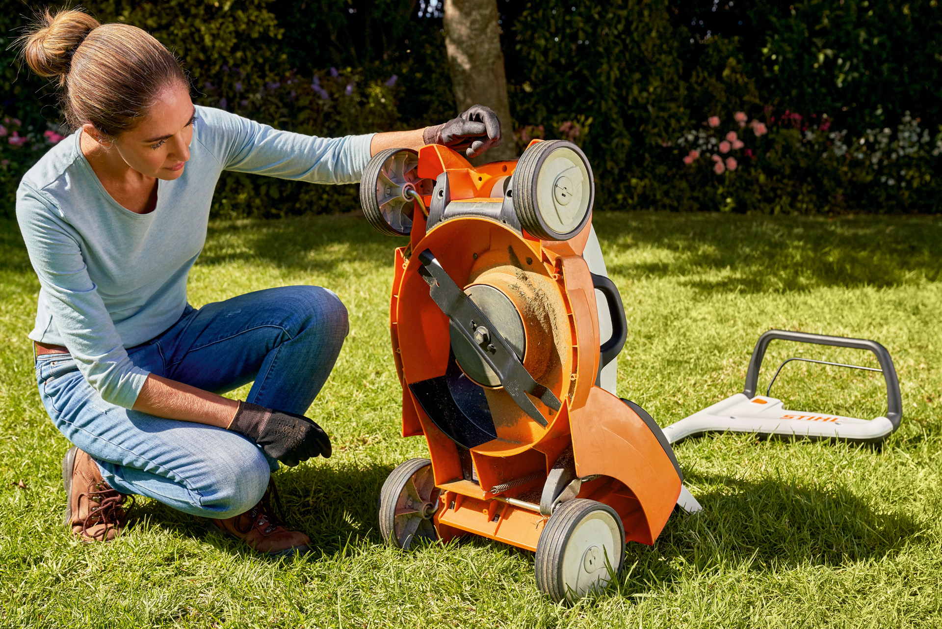 Kobieta zaglądająca pod swoją akumulatorową kosiarkę STIHL RMA 339C w ogrodzie 