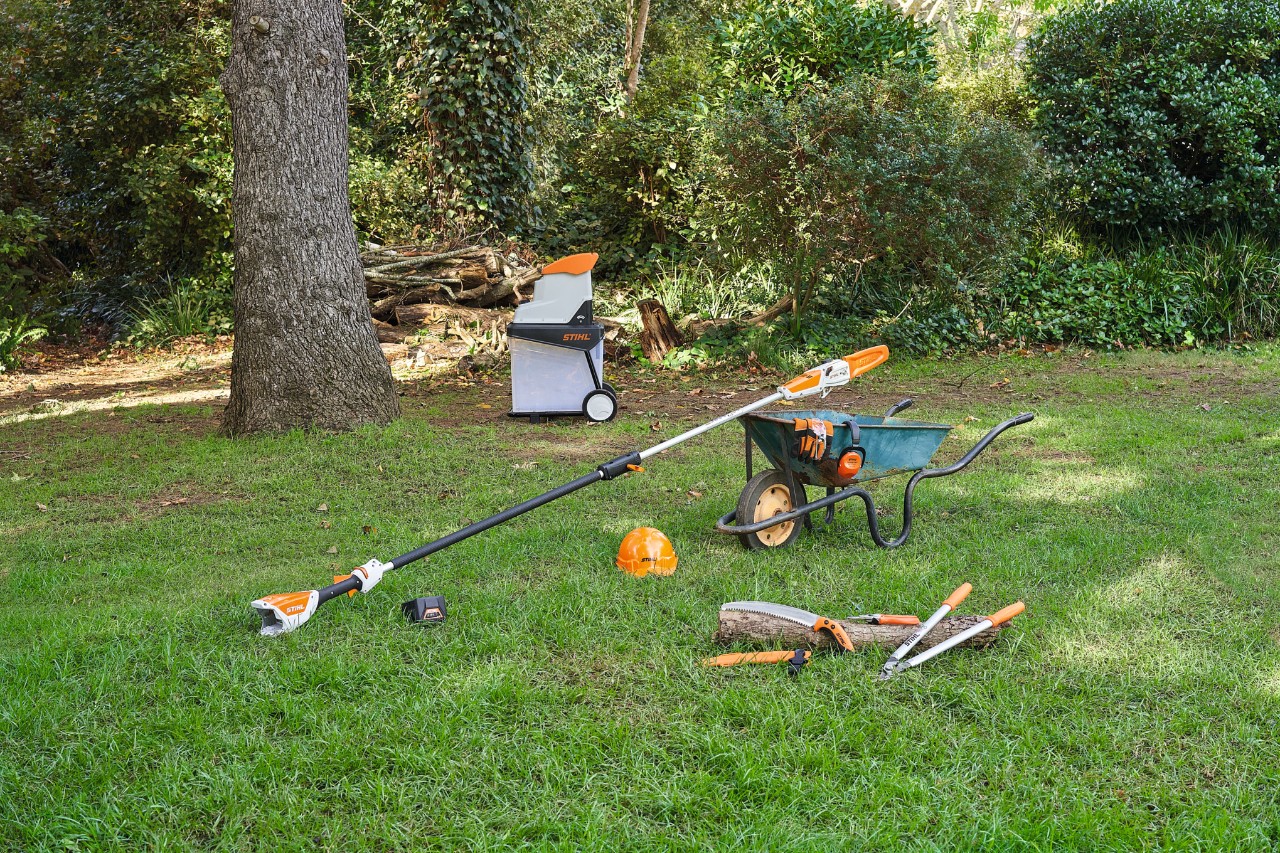 Różne urządzenia, na przykład nożyce ogrodowe i sekatory do gałęzi STIHL, leżące na trawniku w ogrodzie w celu przycięcia jabłoni