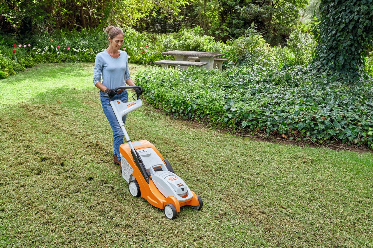 Kobieta chce odnowić trawnik, a więc najpierw kosi go akumulatorową kosiarką STIHL RMA 339 C 
