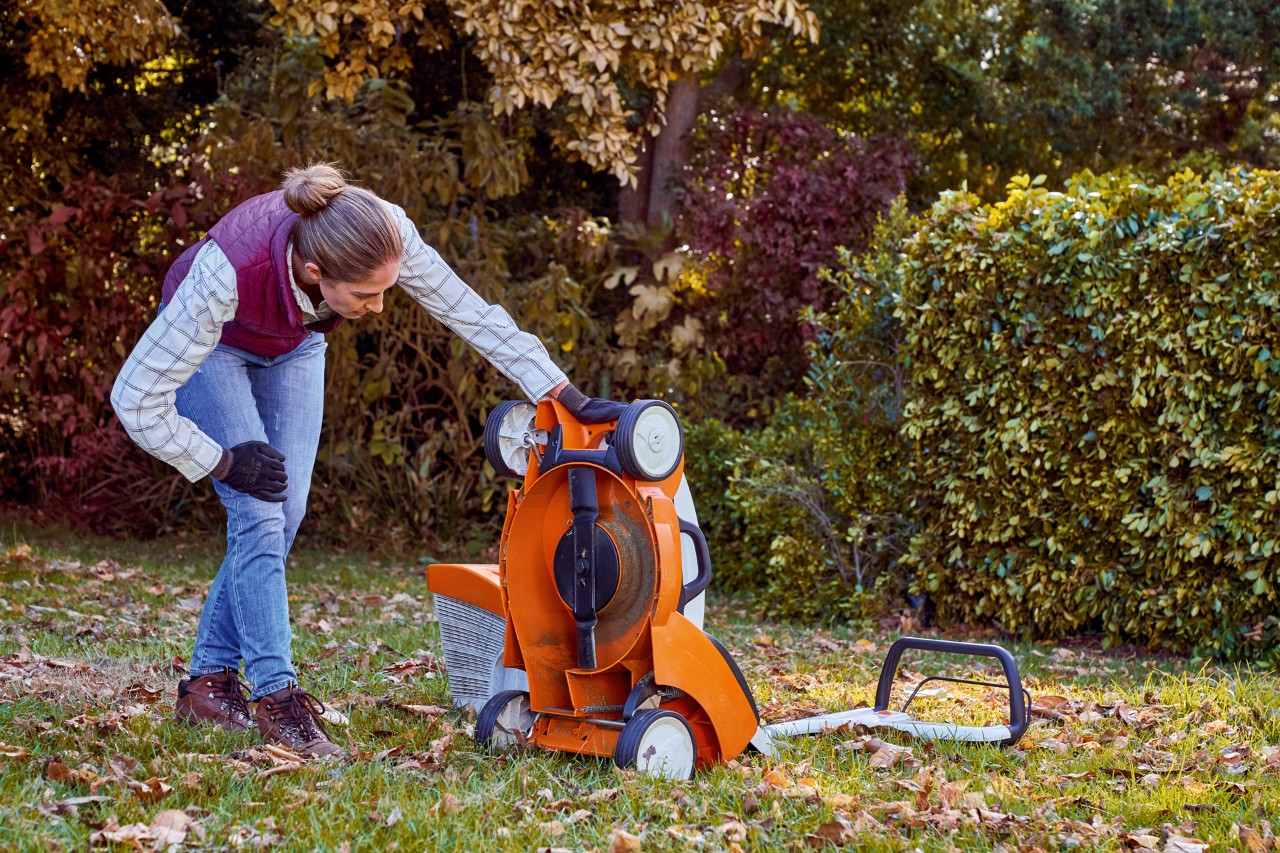 Kobieta sprawdzająca spód kosiarki STIHL RMA 339 C w ramach konserwacji sprzętu po sezonie