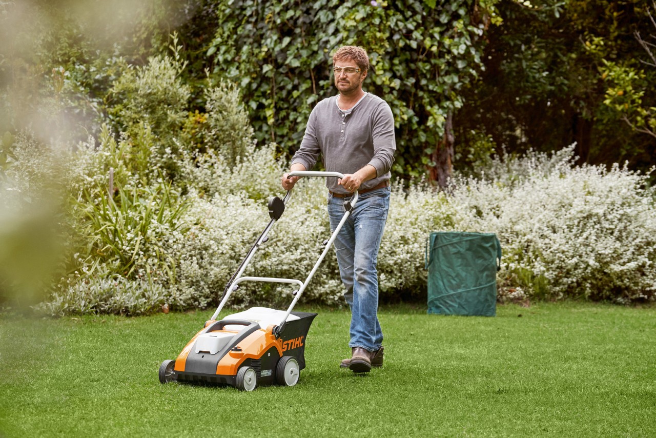 Mężczyzna wertykuluje zielony trawnik za pomocą wertykulatora akumulatorowego STIHL RLA 240