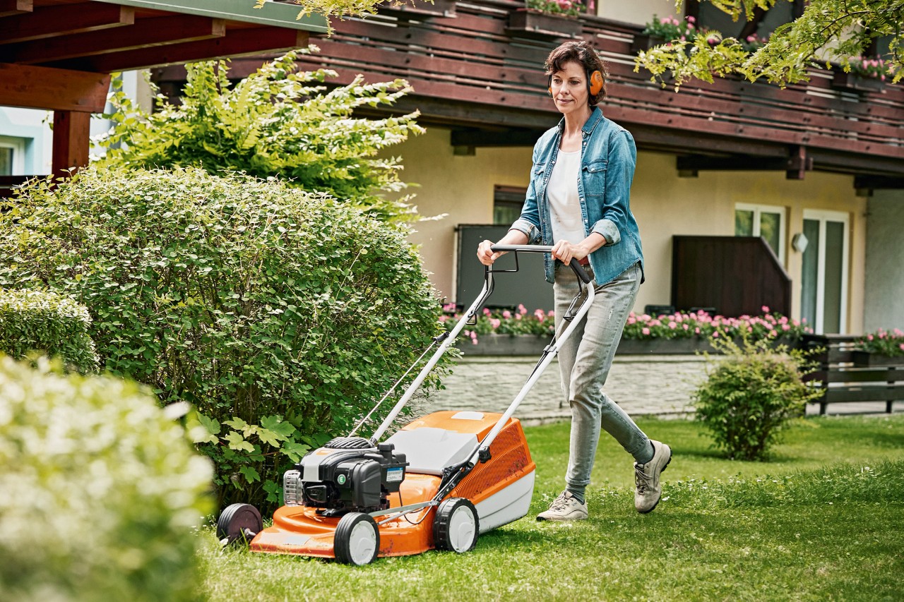 Kobieta pielęgnująca trawnik wiosną za pomocą benzynowej kosiarki STIHL RM 243 T w ogrodzie przed domem