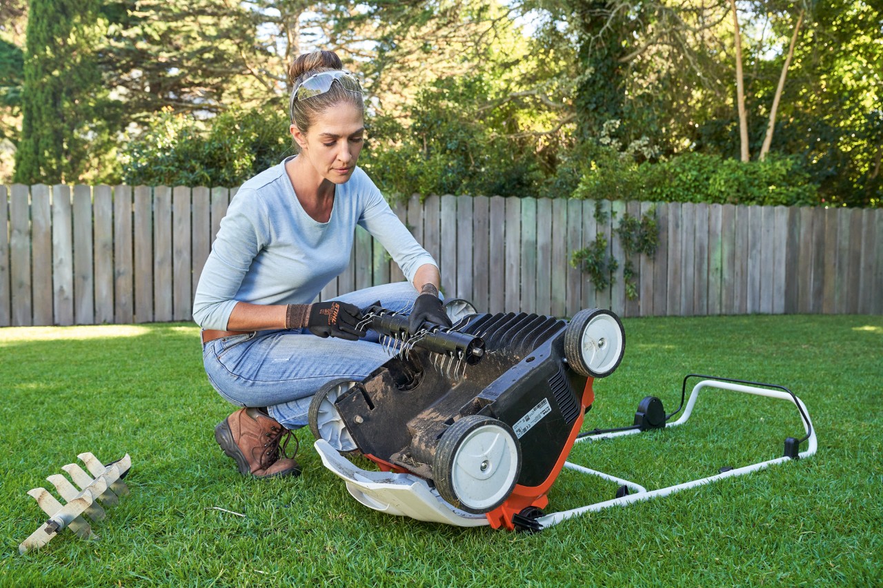 Kobieta w okularach ochronnych i rękawicach roboczych wymienia zespół wertykulatora w akumulatorowym aeratorze do trawnika STIHL RLA 240