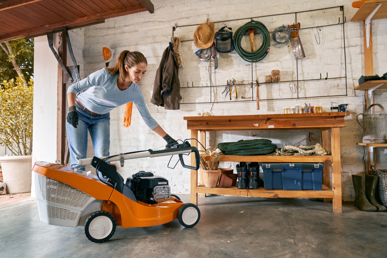 Kobieta przygotowuje kosiarkę benzynową STIHL RM 448 TC do przechowania w garażu na zimę