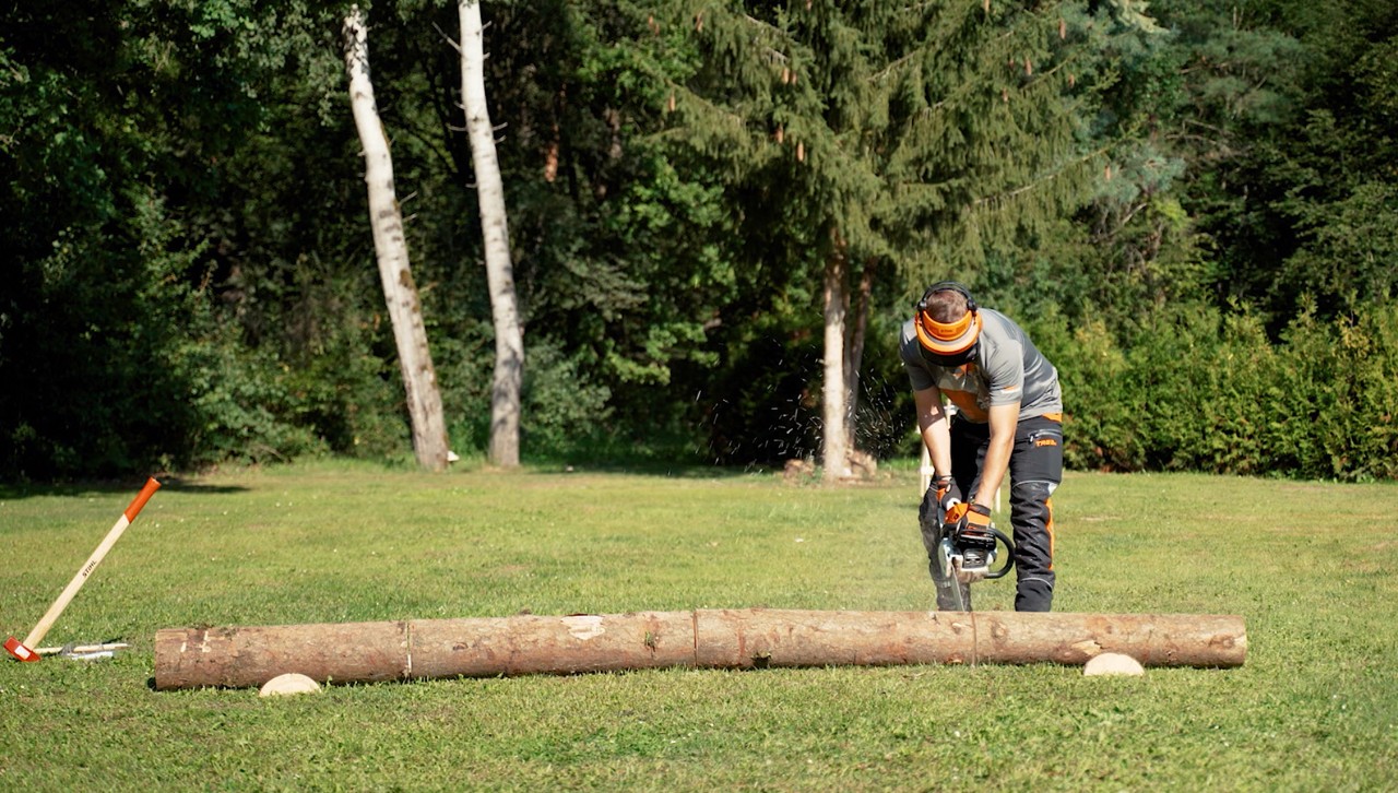 Osoba nosząca sprzęt ochronny używa piły łańcuchowej STIHL do przecięcia pnia drzewa na drewno opałowe
