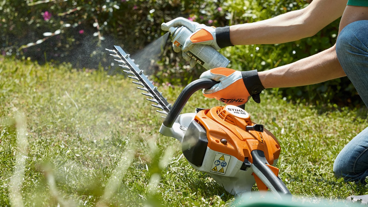 Benzynowe nożyce do żywopłotu STIHL HS 82 T są spryskiwane na zielonym trawniku w celu ich oczyszczenia