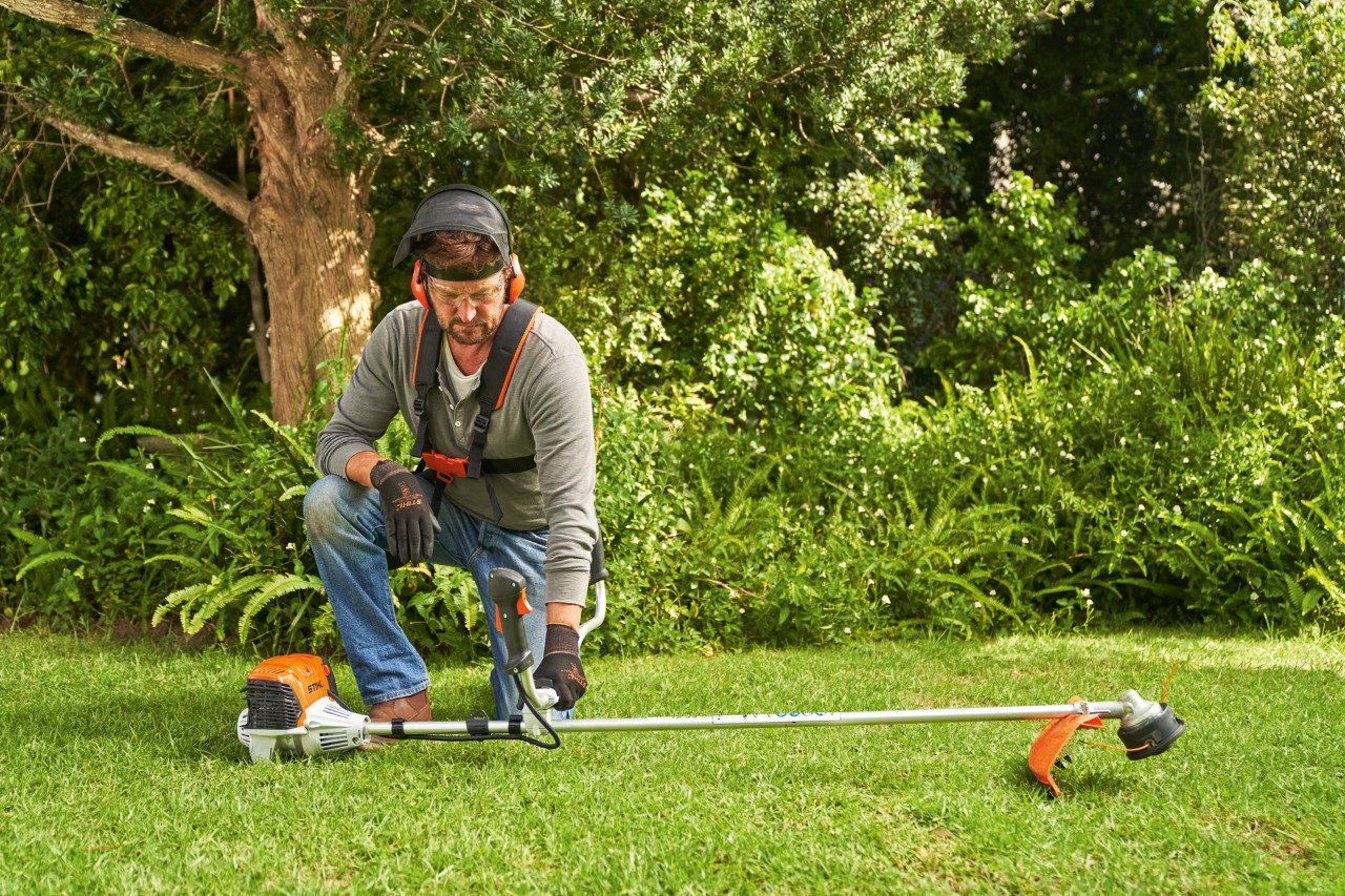 Mężczyzna umieszcza benzynową kosę mechaniczną STIHL FS 91 na ziemi, aby ją uruchomić
