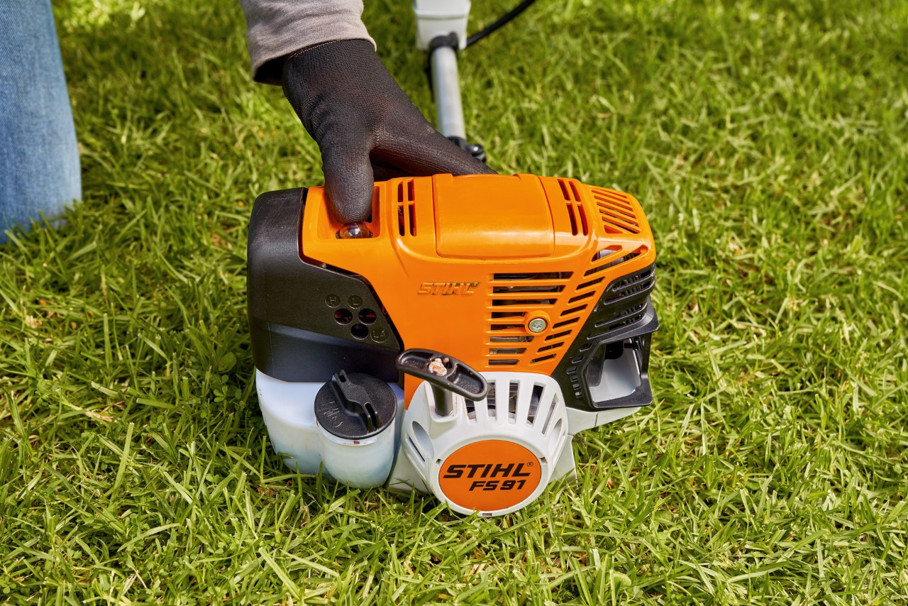 Mężczyzna naciskający pompę paliwa benzynowej kosy mechanicznej STIHL FS 91, aby ją uruchomić