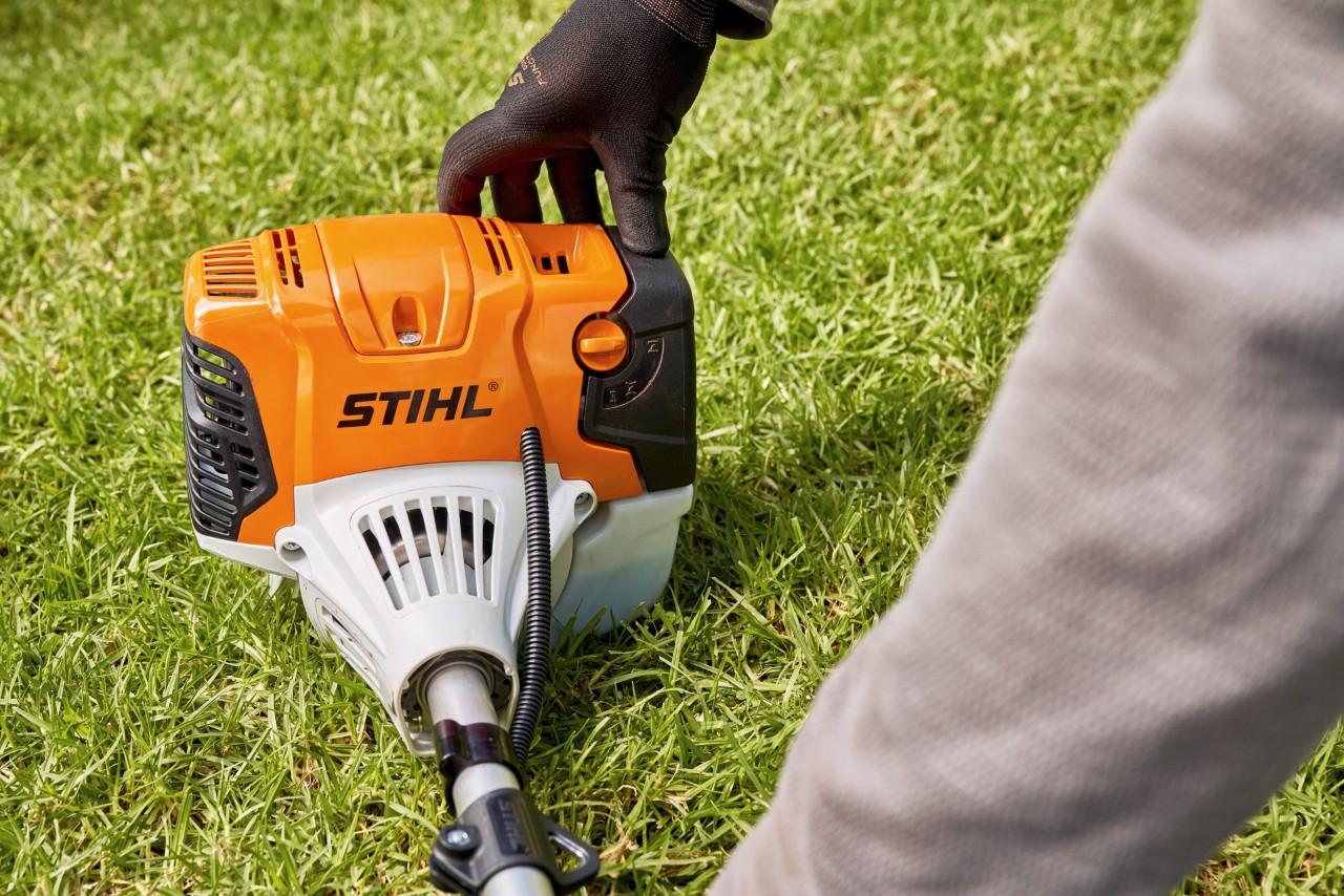 Mężczyzna mocno dociska benzynową kosę mechaniczną STIHL FS 91 do podłoża