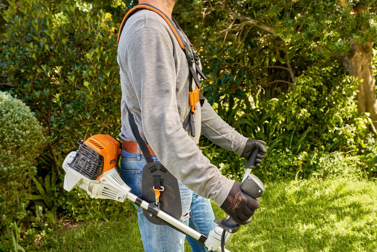 Mężczyzna podnosi benzynową kosę mechaniczną STIHL FS 91 z ziemi, aby rozpocząć koszenie 