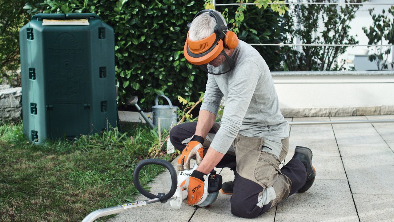 Benzynowa kosa mechaniczna STIHL FS 38 jest dociskana do podłoża przez osobę w odzieży ochronnej