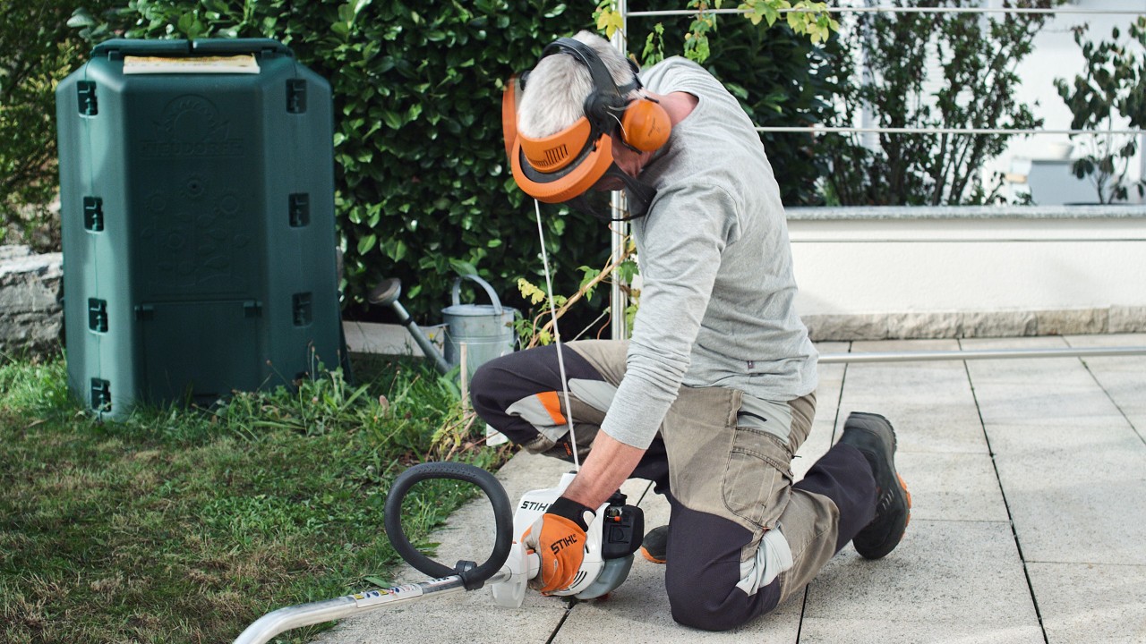 Osoba w odzieży ochronnej ponownie ciągnie linkę rozrusznika benzynowej kosy mechanicznej STIHL FS 38