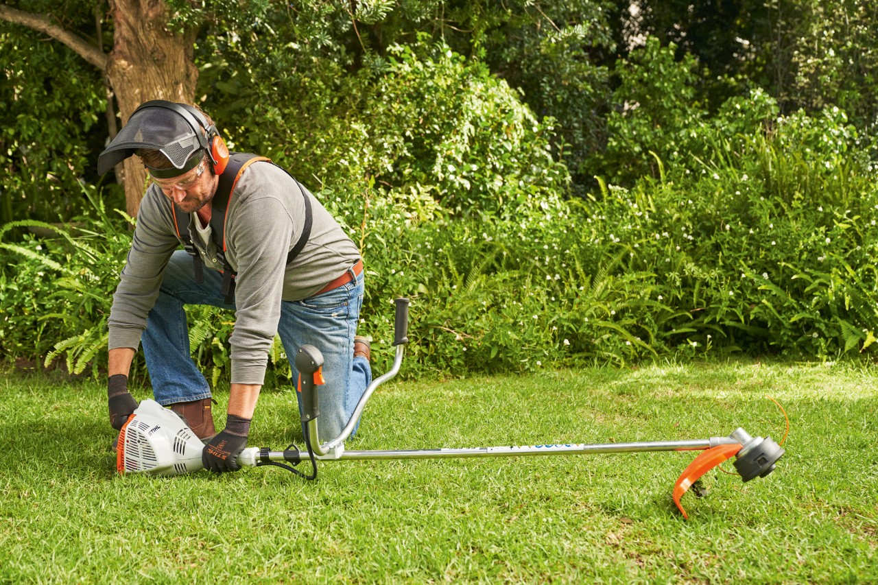 Mężczyzna dociska benzynową kosę mechaniczną STIHL FS 56 do ziemi, aby ją uruchomić