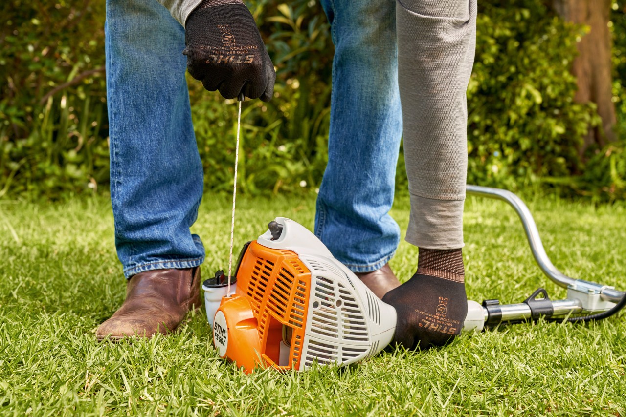 Mężczyzna pociąga linkę rozrusznika benzynowej kosy mechanicznej STIHL FS 56 