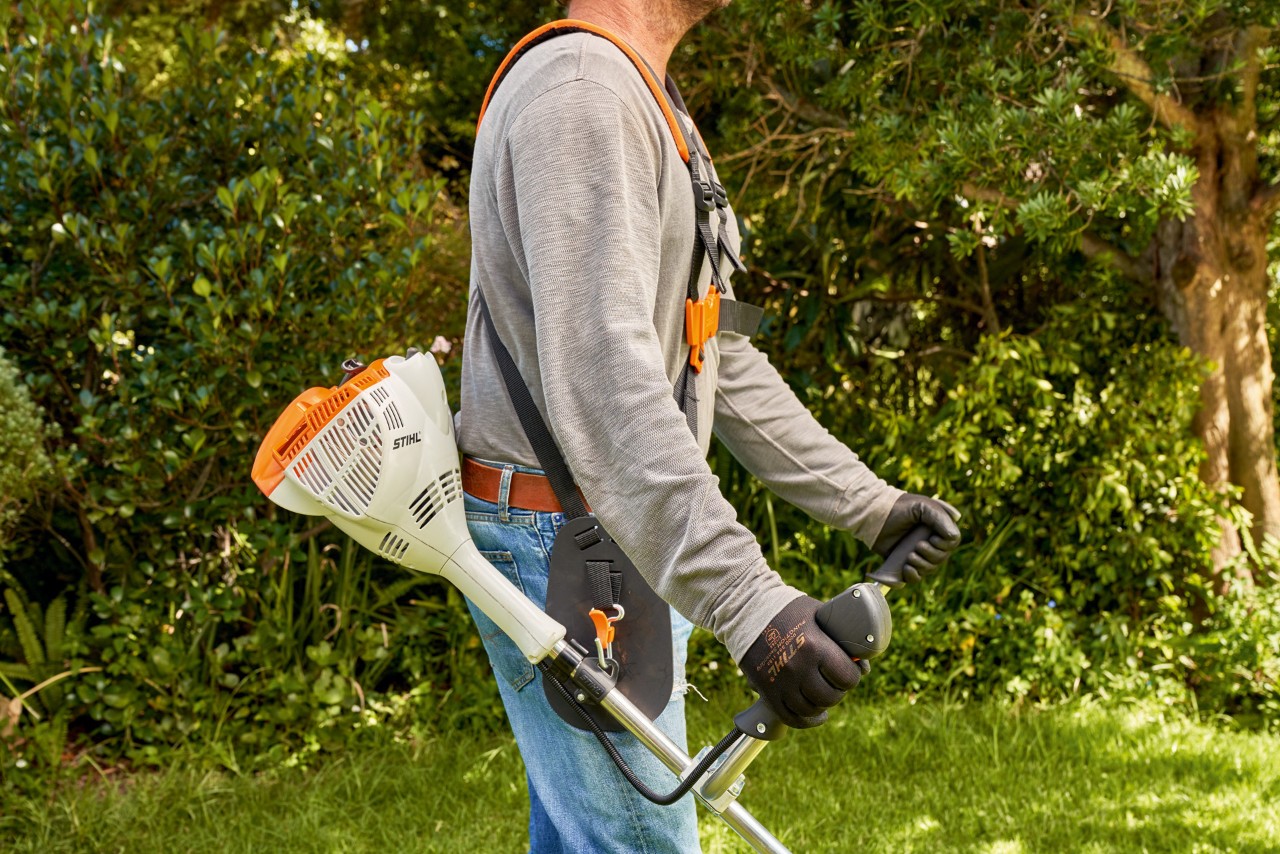 Mężczyzna podnosi benzynową kosę mechaniczną STIHL FS 56 z ziemi