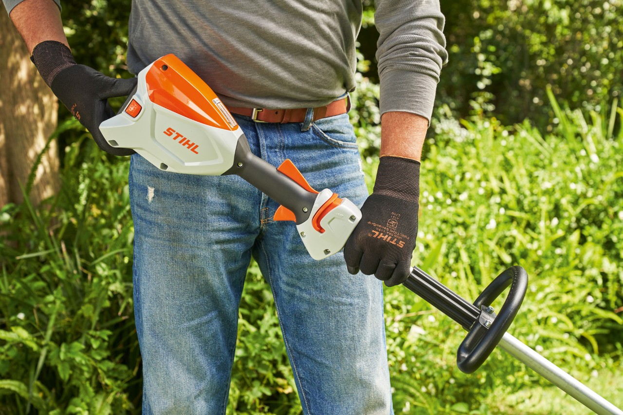 Mężczyzna w rękawicach ochronnych sprawdza akumulator akumulatorowej kosy mechanicznej STIHL FSA 60 przed jej uruchomieniem