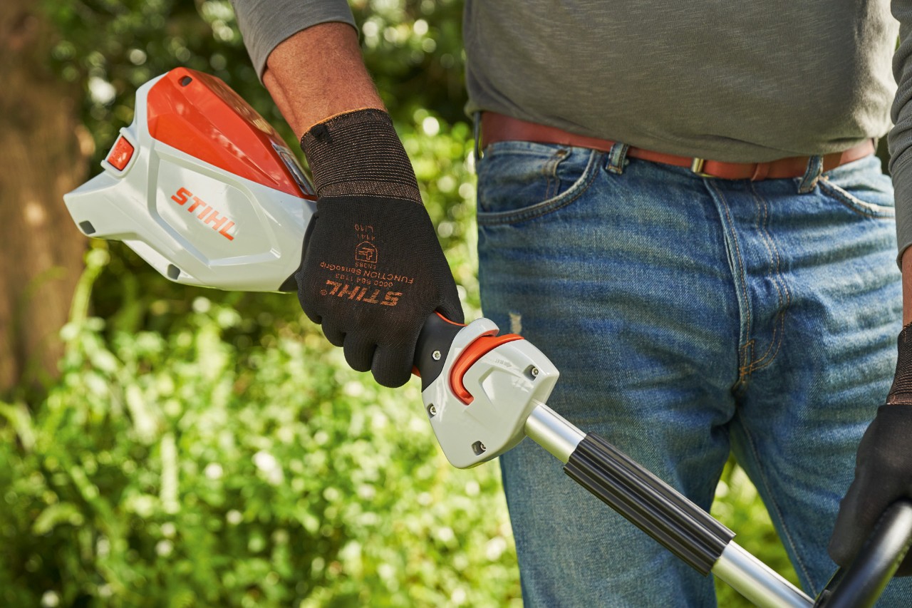 Mężczyzna w rękawicach ochronnych naciska dźwignię zmiany prędkości w akumulatorowej kosie mechanicznej STIHL FSA 60, aby ją uruchomić