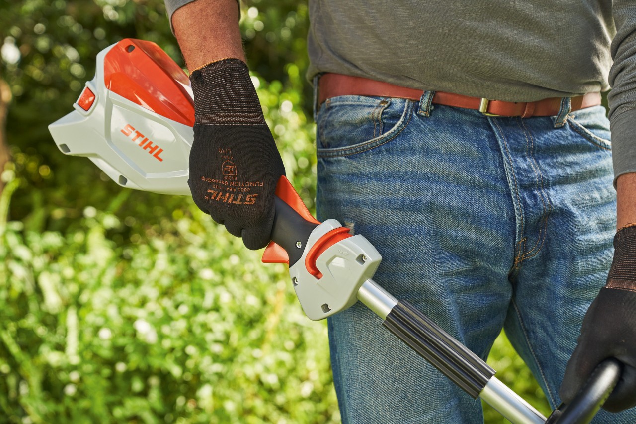 Mężczyzna w rękawicach ochronnych zwalnia dźwignię zmiany prędkości akumulatorowej kosy mechanicznej STIHL FSA 60, aby ją wyłączyć