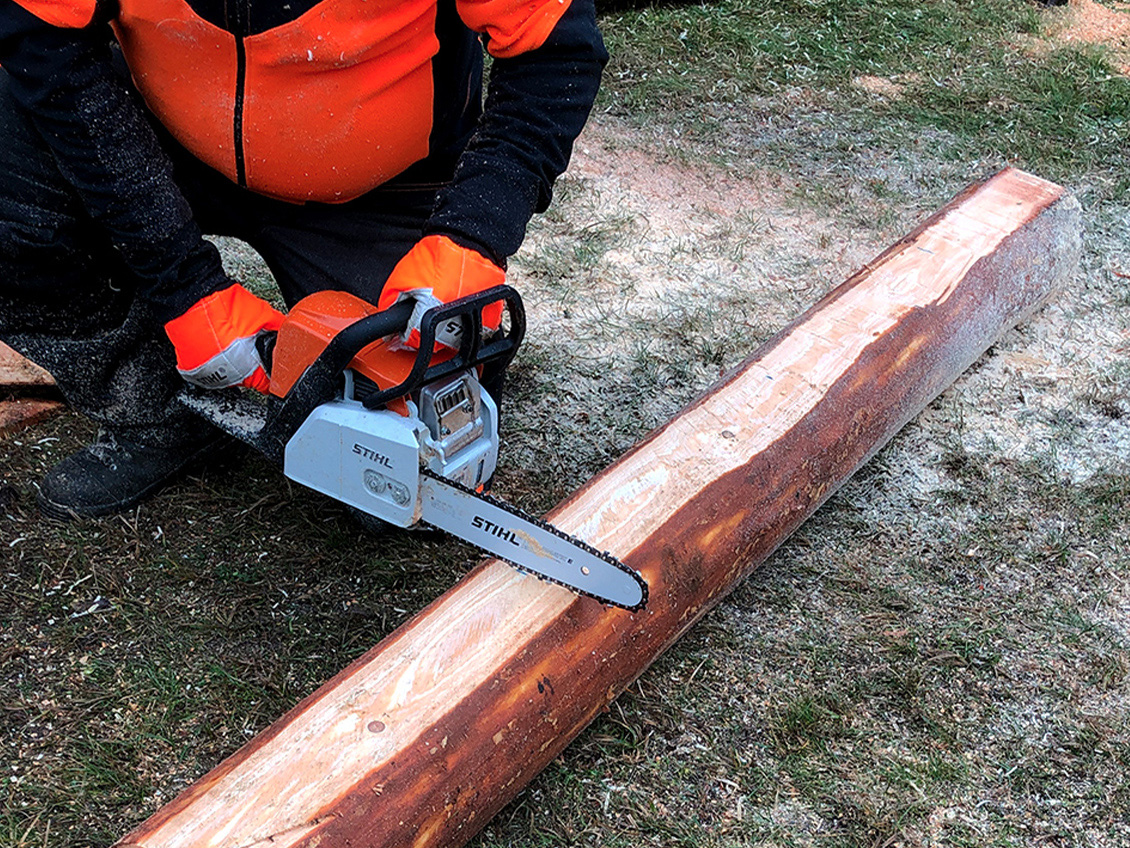  Osoba w odzieży ochronnej przycinająca pień pilarką łańcuchową STIHL