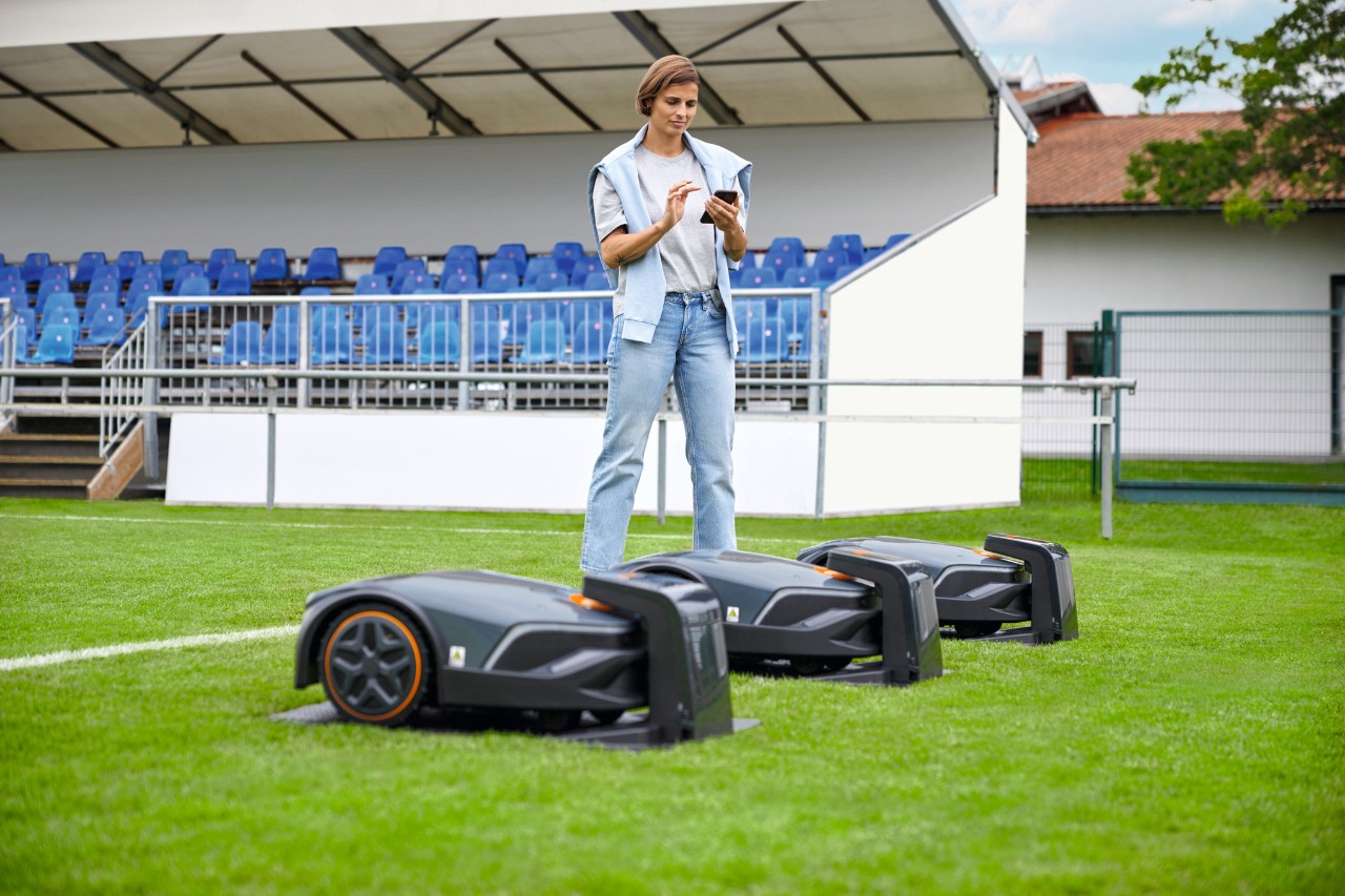 Kobieta za pomocą aplikacji mobilnej zarządza zespołem 3 robotów STIHL iMOW® 7 Pro.