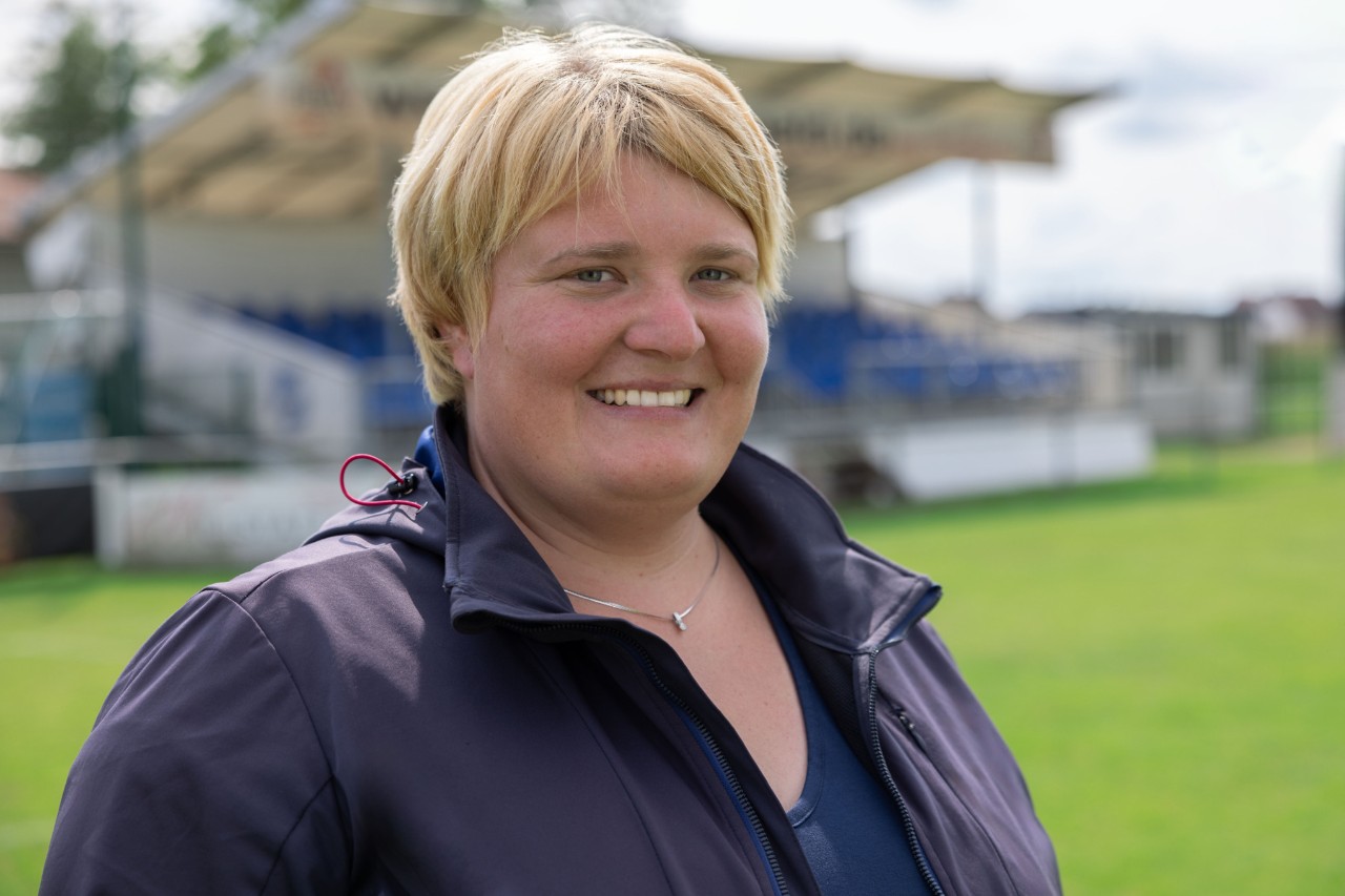Lesly Huber, odpowiedzialna za pielęgnację zieleni, stoi na boisku sportowym klubu SC Sand i uśmiecha się do kamery
