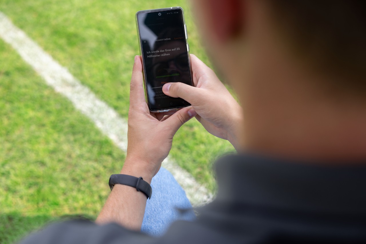 Osoba na boisku sportowym otwiera aplikację MY iMOW® na telefonie komórkowym