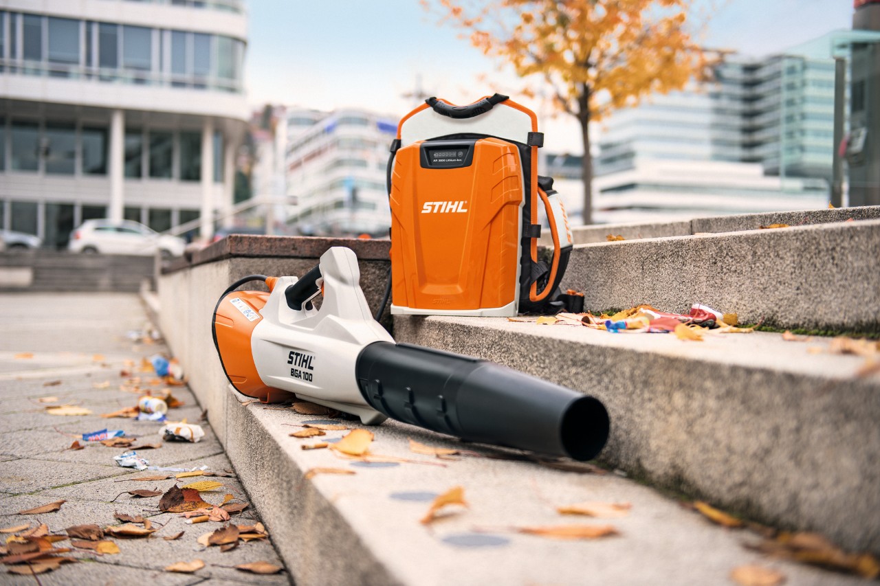 Na kamiennych schodach pokrytych liśćmi leżą akumulatorowa dmuchawa do liści STIHL BGA 100 i profesjonalny akumulator plecakowy STIHL AR 3000 L