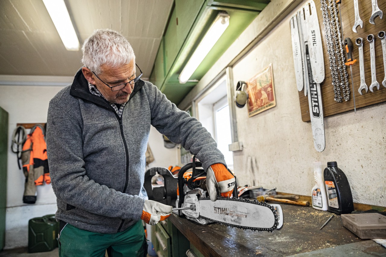 Mężczyzna w warsztacie skręca pilarkę spalinową z prowadnicą STIHL Rollomatic E 