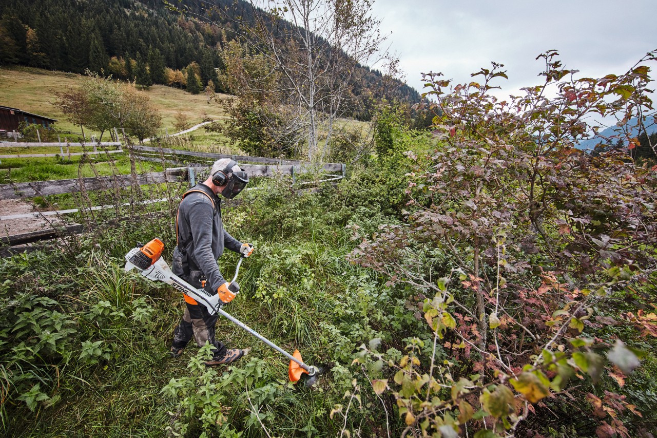 Mężczyzna w ubraniu ochronnym kosi gęste zarośla kosą spalinową STIHL FS 311