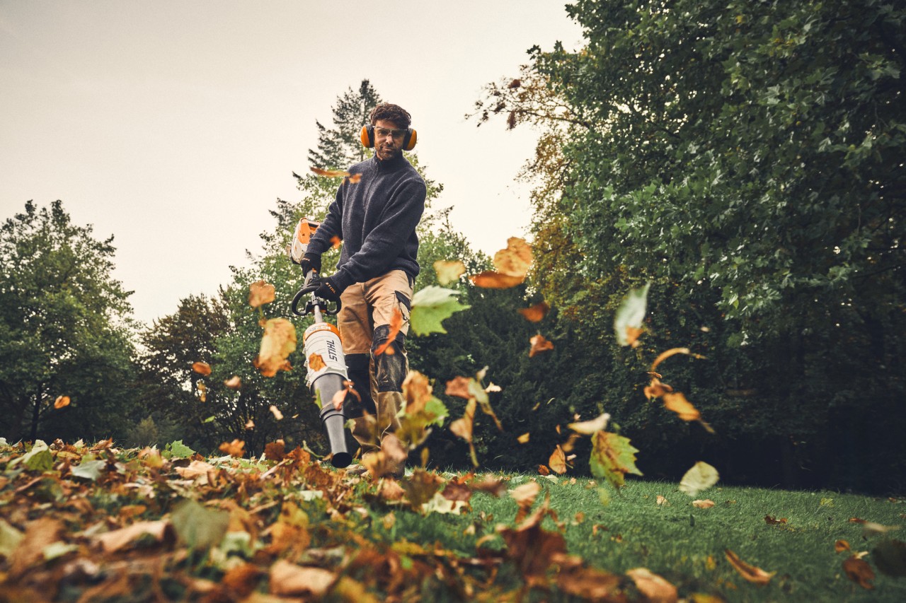 Mężczyzna usuwa liście za pomocą akumulatorowej kosy spalinowej STIHL KMA 200 R.