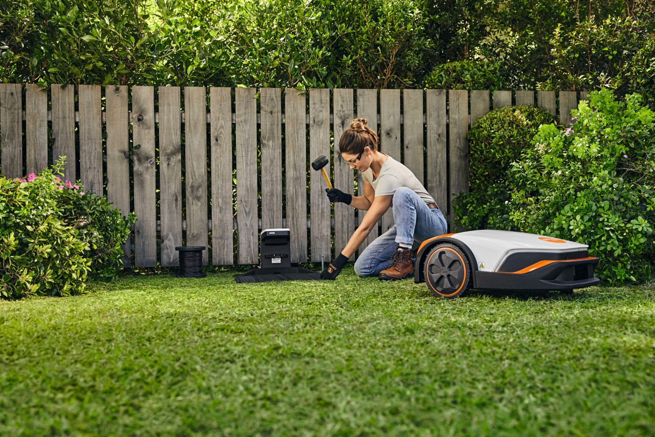 Kobieta instaluje stację dokującą STIHL iMOW® przed ogrodzeniem w swoim ogrodzie.